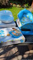Photo showing the blue baby bather with aquatic-themed fabric, the microwave sterilizer, and the product box with branding and instructions.