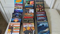 Photo showing 25 DVD movies stacked on a chair, titles visible including Lethal Weapon, Bad Boys, Seinfeld, Pirates of the Caribbean.