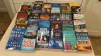 Photo showing all 30 paperback books laid out on a table, titles visible including Broken Ice by Matt Goldman, Wrath of Poseidon by Clive Cussler, and more.