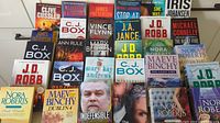Books with visible spines showing a variety of authors and titles including Clive Cussler, J.D. Robb, Nora Roberts, and Maeve Binchy.