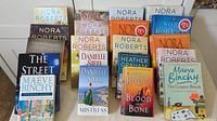 Twenty paperback novels arranged standing and laying down showing front covers with emphasis on author names.