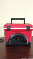 Front view of red mini cooler with black handle, black front panel for radio controls, white trim and latches.