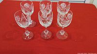 Top view of 6 crystal wine glasses arranged in two rows on a red surface, showing pinwheel cut patterns on the bowls.