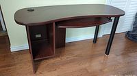 Full view of the kidney-shaped dark wood desk, showing the pullout keyboard shelf extended and an open shelf underneath with wire cutouts