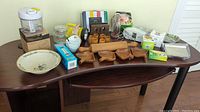 Wide shot of the lot showing all items on a wooden table, featuring boxed Pampered Chef chopper, a pepper grinder box, wooden kitchenware, glass jar, and ceramic dish.