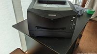 Lexmark laser printer front view showing paper output tray extended on black finish plastic body.