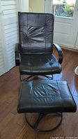 Front view of black artificial leather swivel chair with matching footstool, showing tufted cushion details and circular metal bases