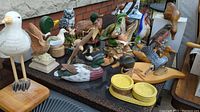 Wide view of about two dozen carved bird and duck figures on a table showing variety of species and materials.