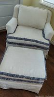 Front view of cream textured occasional chair with matching footstool showing fringe trim and cushion details.