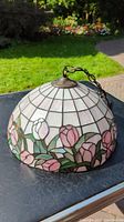 Side view of Tiffany-style stained glass light fixture on table outdoors showing pink and green floral patterns on dome shade.