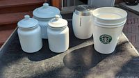 Photo showing all six items: three white ceramic canisters with lids and three Starbucks containers (two white plastic cups with logo, one metal canister)
