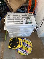 Front view of LG window air conditioner unit with remote and 12/2 Romex cable roll on floor, along with yellow power cord reel.