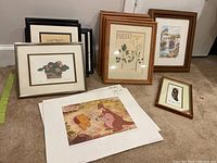 Wide view of collection showing multiple framed artworks arranged on floor, includes botanical prints, Disney art prints, and various framed traditional paintings