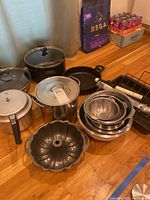 Full view of cookware including Calphalon pots, aluminum bowls, Bundt pan, grilling utensils, and roasting pan on wood floor.