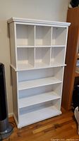 Front view of white wooden bookshelf showing 8 top cubbies and 3 lower shelves