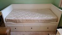 Full view of white wooden daybed showing mattress and three drawer storage beneath