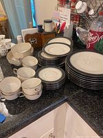 Photo showing cups, saucers, dinner and salad plates stacked on a counter with other kitchen items