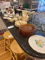 Full lot view on kitchen countertop showing the varied plates, teapot set, glassware, and decorative rooster