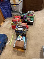 Photo showing assorted board and card games stacked in boxes and plastic storage bins in background.