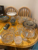 Photo showing a collection of various glassware and crystal pieces arranged on a wooden table including candy dishes, bowls, cake plate, relish tray, and bread dish.