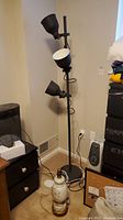 Full view of black floor lamp with three movable cone-shaped shades beside white and gold floral table lamp base
