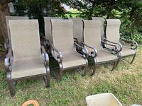 Four identical outdoor sling chairs arranged side by side on grass beneath a tree