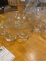 Clear glass punch bowl with matching glass ladle and 11 small punch glasses arranged around it on a wooden table.