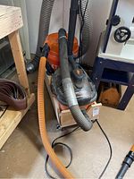 Full view of RIDGID Portable Vac connected to orange dust separator with hoses and cord visible, positioned near wooden bench and blue machinery.