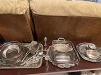 Full view of all silver plated serving ware including trays, candlesticks, spoons, bowls, and butter dish, showing overall condition.