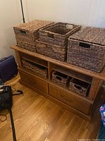 Wood storage cabinet with six wicker baskets placed on and inside the cubbies. Shows top, drawers and baskets.