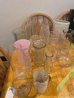 Overview of multiple vases of various sizes, colors and materials placed on a wooden table.