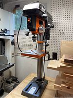 Front view of drill press on wooden workbench showing cast iron base, column, adjustable table, head assembly