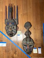 Two hand-carved African tribal masks displayed on wooden floor showing the size and details.