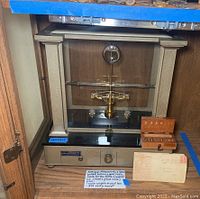 Front view of the gold scale with metal and glass case, showing weights and receipt placed in front.