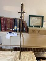 Full view of sword sheathed in scabbard against bookshelves