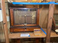 Full frontal view of wooden and glass case housing the brass button balance scale alongside the wooden box of weights