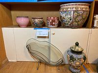 Shelf display with four ceramic pots, one large pottery urn, glass dish with metal stand