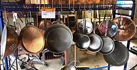 Copper pots, pans, and cooking implements hanging on metal rack. Assorted sizes and shapes visible, including colanders and frying pans.