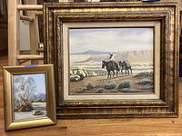 Two framed desert landscape paintings with the smaller painting placed in front of the larger one.
