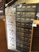 Photo showing two vintage metal filing cabinets side by side, one gray with multiple shallow drawers and one white with fewer but deeper drawers.