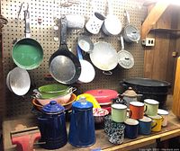 Wide shot showing most items in the lot including enamel pots, strainers, mugs, coffee pots, and pans displayed on a pegboard and workbench.