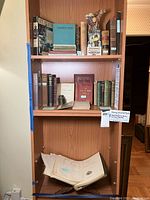 Three-shelf wooden bookshelf displaying entire lot of books, manuals, decanter, and map