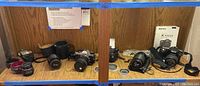 Overview of lot showing three camera bodies, lenses including Vivitar, Promaster, Pentax, and Tokina, flash unit, camera cases, and straps arranged on wooden surface.