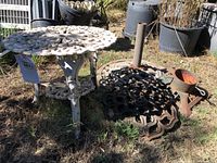Side view of wrought iron garden table and three metal stands showing design and weathered condition