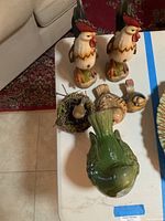 View showing pair of folk art wooden roosters, small nest, and three small bird figurines on a white table.