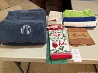 All towels arranged on white table: monogrammed navy bath towels, striped beach towel, Vermont kitchen towel, holiday and floral kitchen towels.