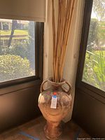 Front view of large decorative pot with bamboo sticks inside, placed near a window corner.