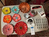 Lot arranged on white table showing colorful ceramic flower plates, two mugs, ice trays, digital thermometer, white candle burner, and bake pan