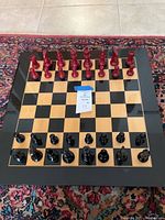 Chess set arranged on a patterned rug, showing the board with red and black pieces placed in starting positions.