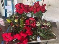 Full view of multiple faux red poinsettia flowers and various Christmas floral arrangements on table in garage